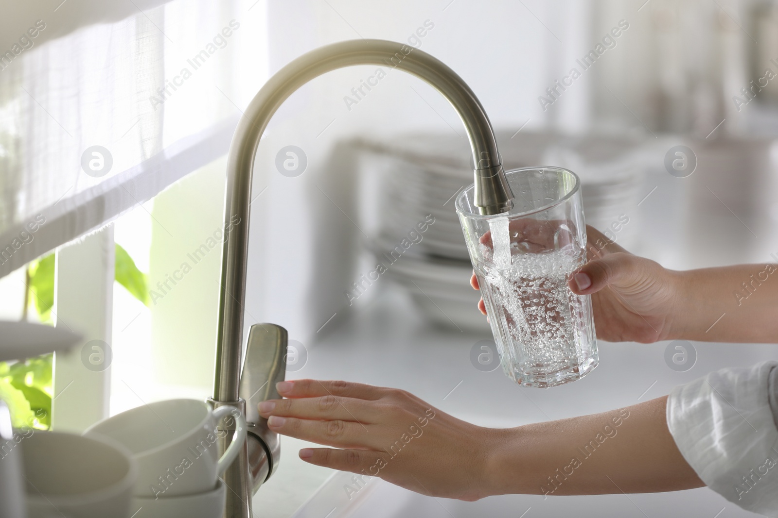 Photo of Woman pouring water into glass in kitchen, closeup