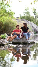 Young happy couple sitting on rock outdoors. Camping vacation