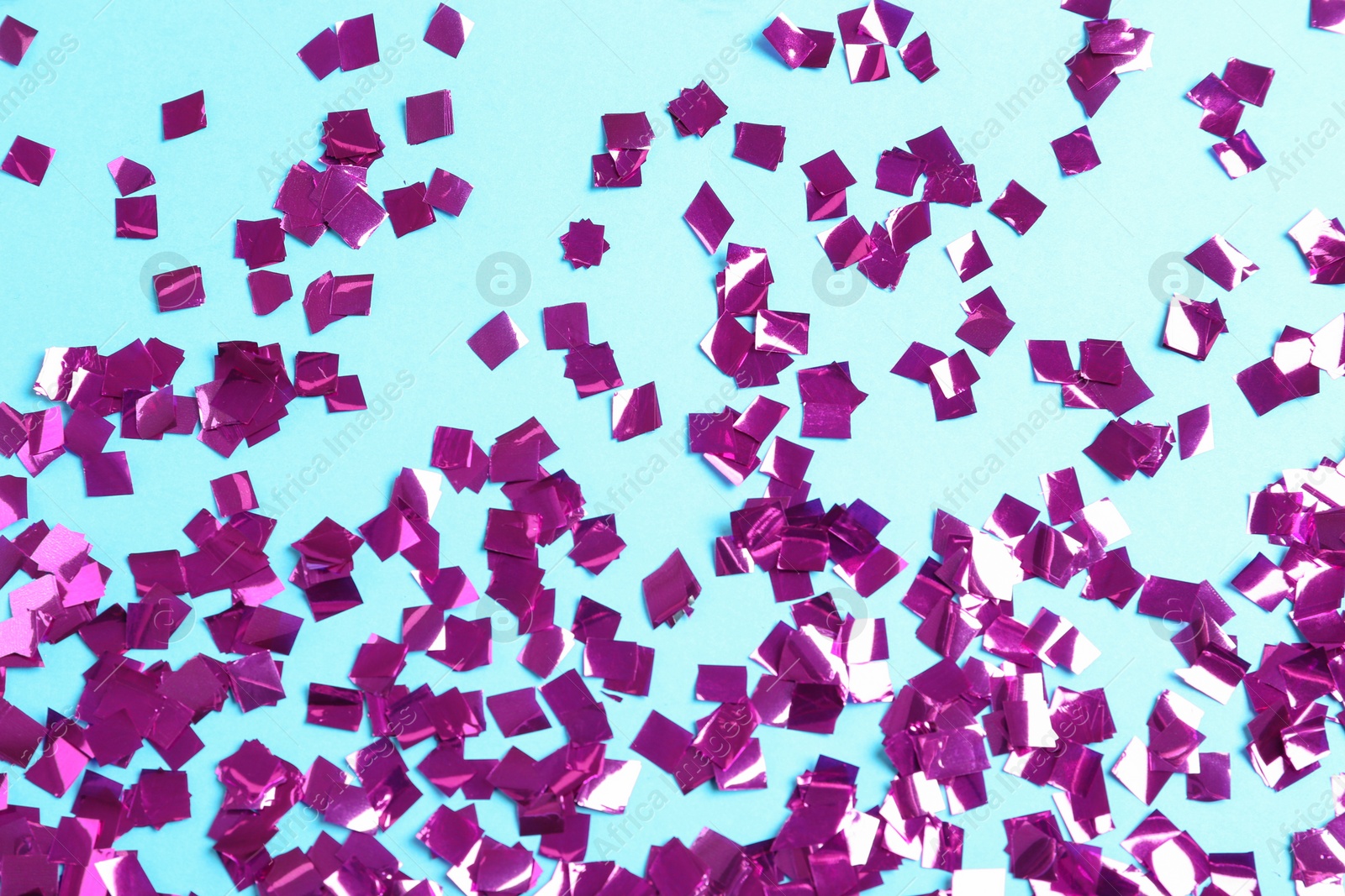 Photo of Shiny purple confetti on light blue background, flat lay
