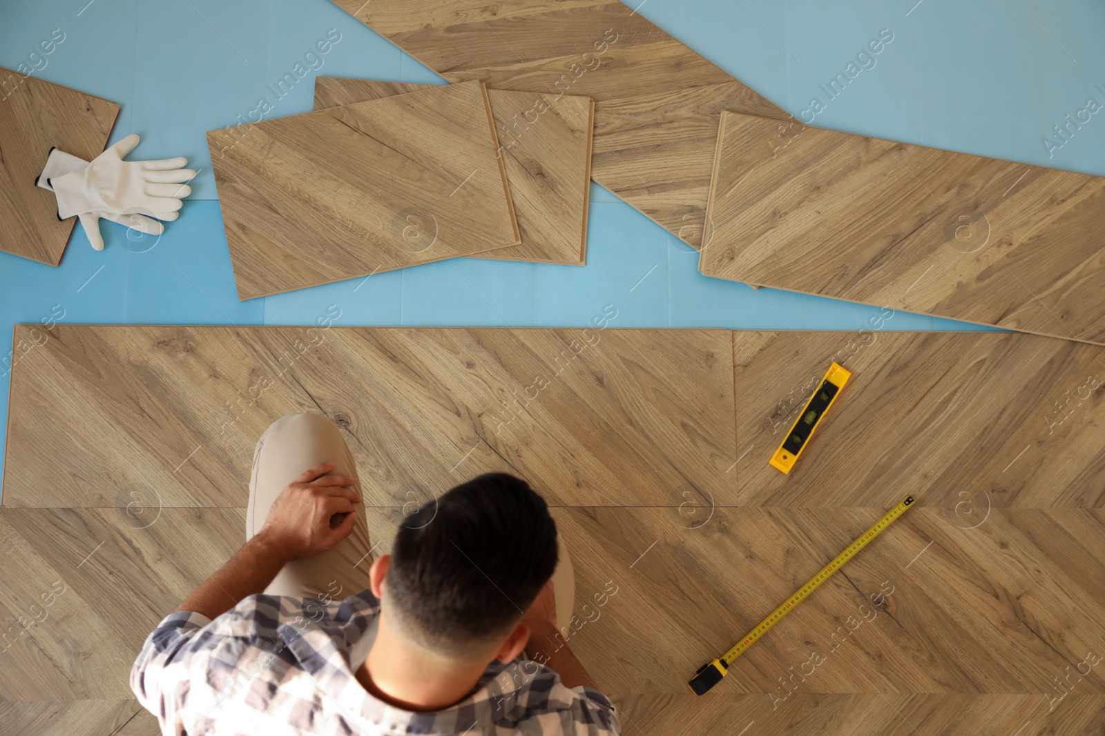 Photo of Professional worker installing new parquet flooring indoors, top view