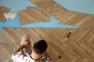 Photo of Professional worker installing new parquet flooring indoors, top view