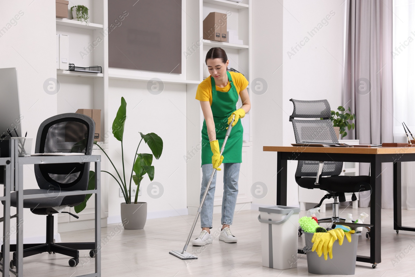 Photo of Cleaning service worker washing floor with mop. Bucket with supplies in office