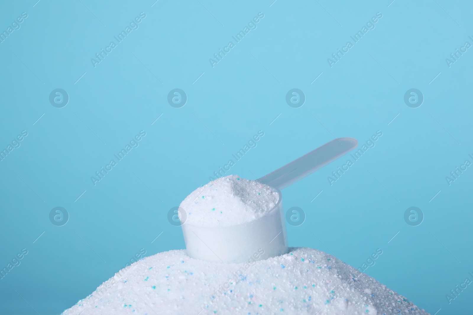 Photo of Pile of laundry detergent and measuring scoop against blue background