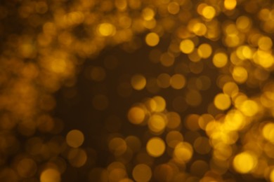 Blurred view of golden glitter on dark background. Bokeh effect