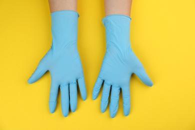Person in medical gloves on yellow background, top view