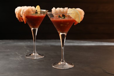 Photo of Tasty shrimp cocktail with sauce in glasses and lemon on grey textured table