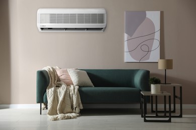 Image of Modern air conditioner on beige wall in room with stylish sofa