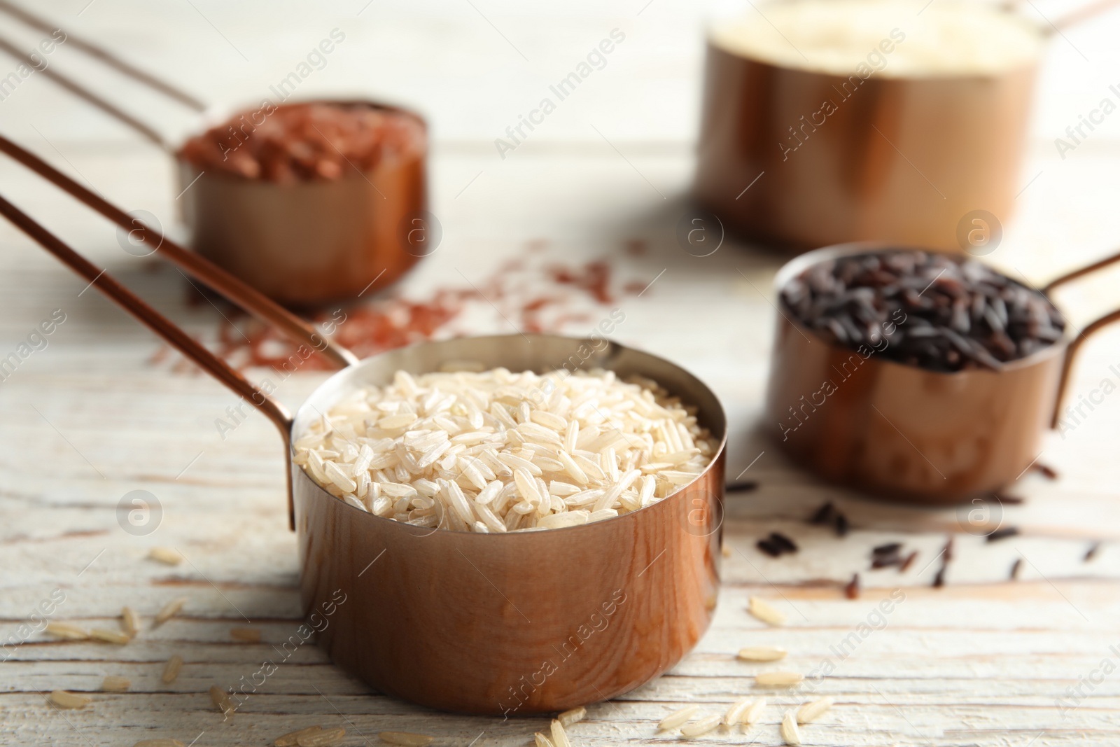 Photo of Measuring cup with different types of rice on white wooden table