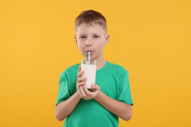 Photo of Cute boy drinking fresh milk from glass on orange background