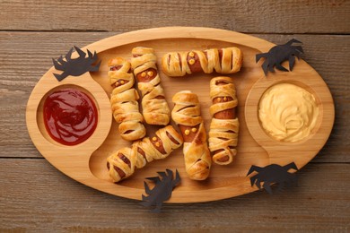 Photo of Cute sausage mummies served with sauce on wooden table, top view. Halloween party food
