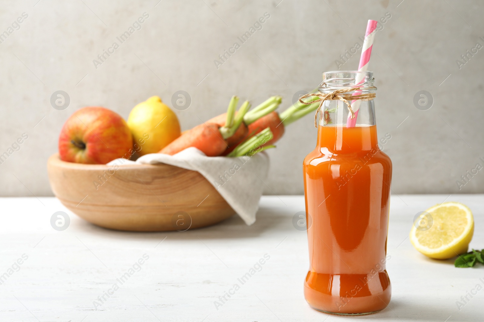 Photo of Bottle of fresh carrot juice and ingredients on white wooden table against light background, space for text
