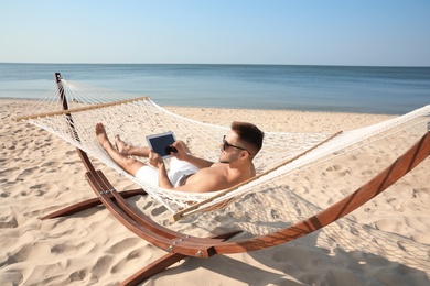 Photo of Young man with tablet in hammock on beach