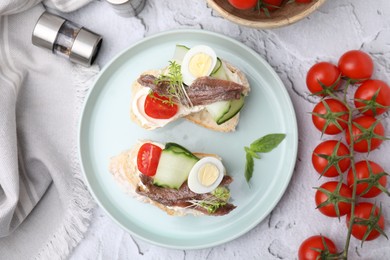 Delicious bruschettas with anchovies, tomato, cucumber, egg and cream cheese on white textured table, flat lay