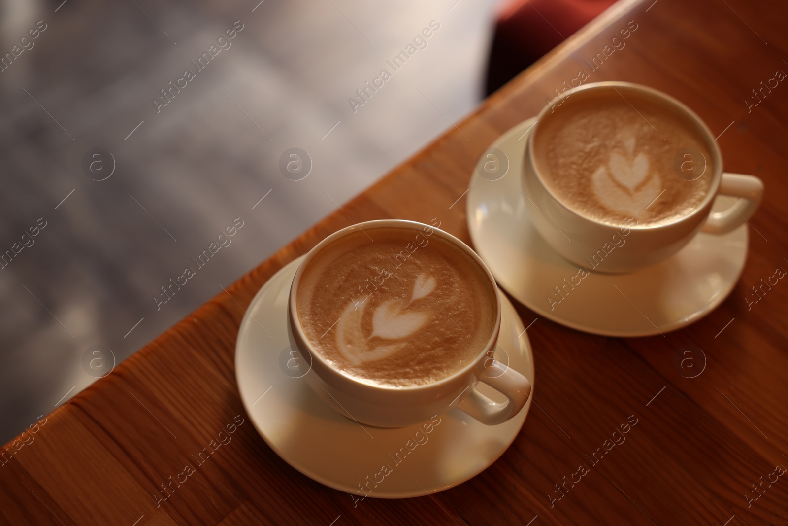 Photo of Cups of aromatic coffee with foam on wooden table in cafe