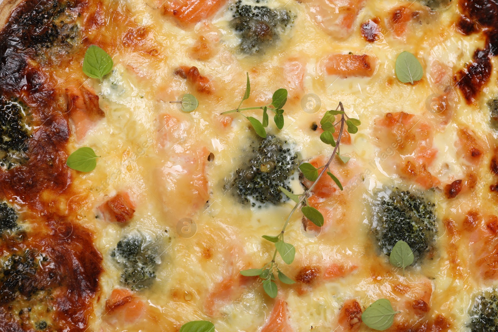 Photo of Delicious homemade quiche with salmon, basil and broccoli as background, top view