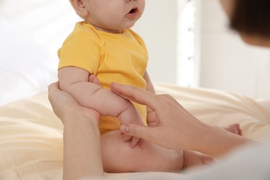 Mother massaging her cute baby with oil on bed at home, closeup