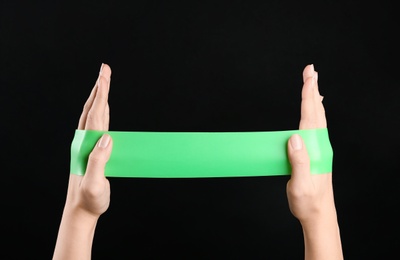 Woman with fitness elastic band on black background, closeup