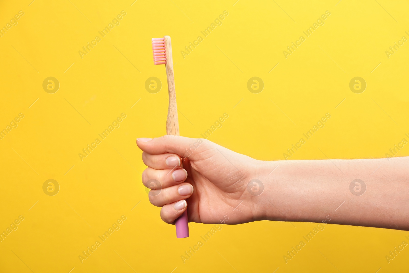 Photo of Woman holding bamboo toothbrush on yellow background, closeup