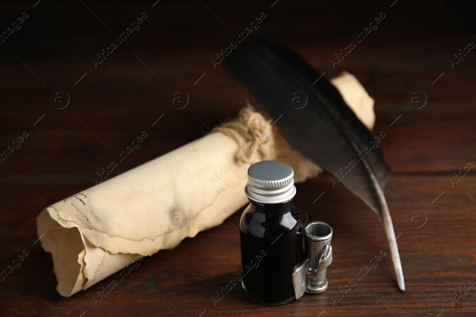 Photo of Feather pen, bottle of ink and parchment scroll on wooden table