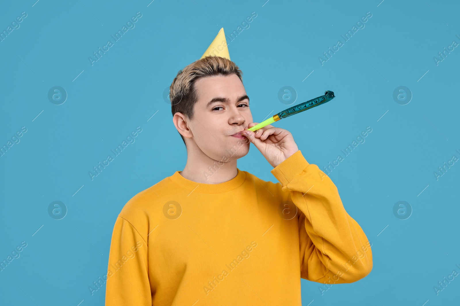 Photo of Young man with party hat and blower on light blue background