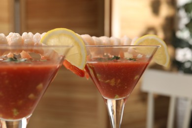 Tasty shrimp cocktail with sauce in glasses and lemon on blurred background, closeup