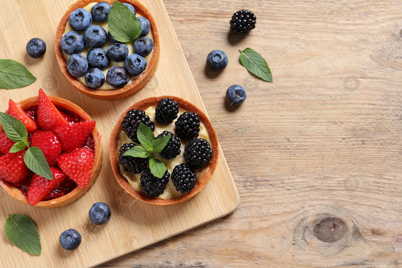 Photo of Tartlets with different fresh berries on wooden table, flat lay and space for text. Delicious dessert