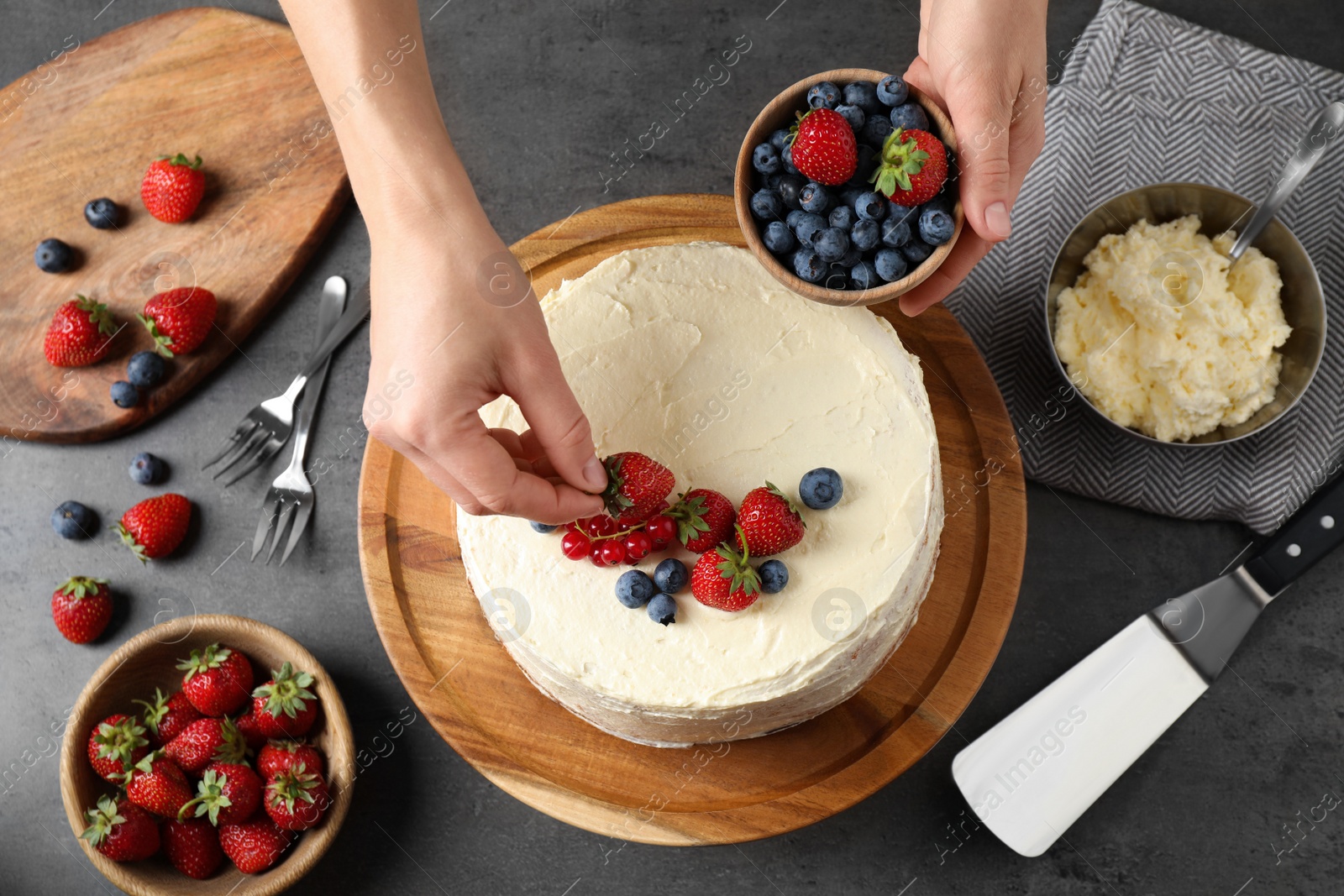 Photo of Woman decorating delicious homemade cake with fresh berries at table, top view