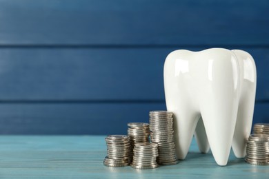Photo of Ceramic model of tooth and coins on light blue wooden table, space for text. Expensive treatment