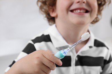 Photo of Little boy holding electric toothbrush indoors, closeup