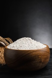 Photo of Wheat flour in bowl on black wooden table, closeup