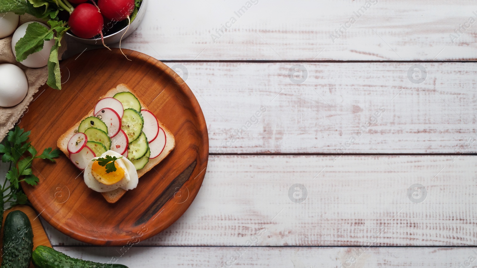 Photo of Tasty sandwich with boiled egg, radish, cucumber and ingredients on white wooden table, flat lay. Space for text