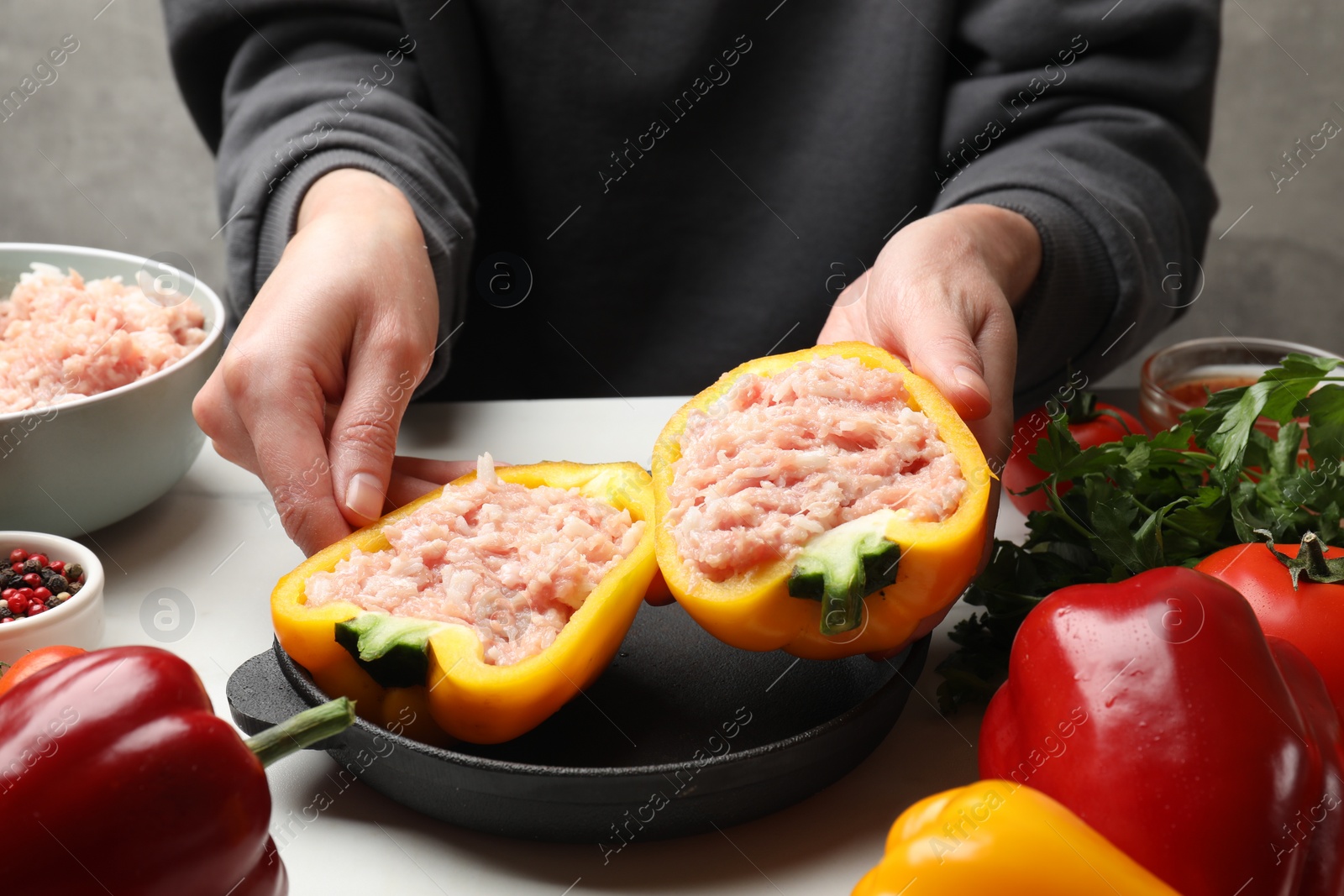 Photo of Woman making stuffed peppers with ground meat at white table, closeup