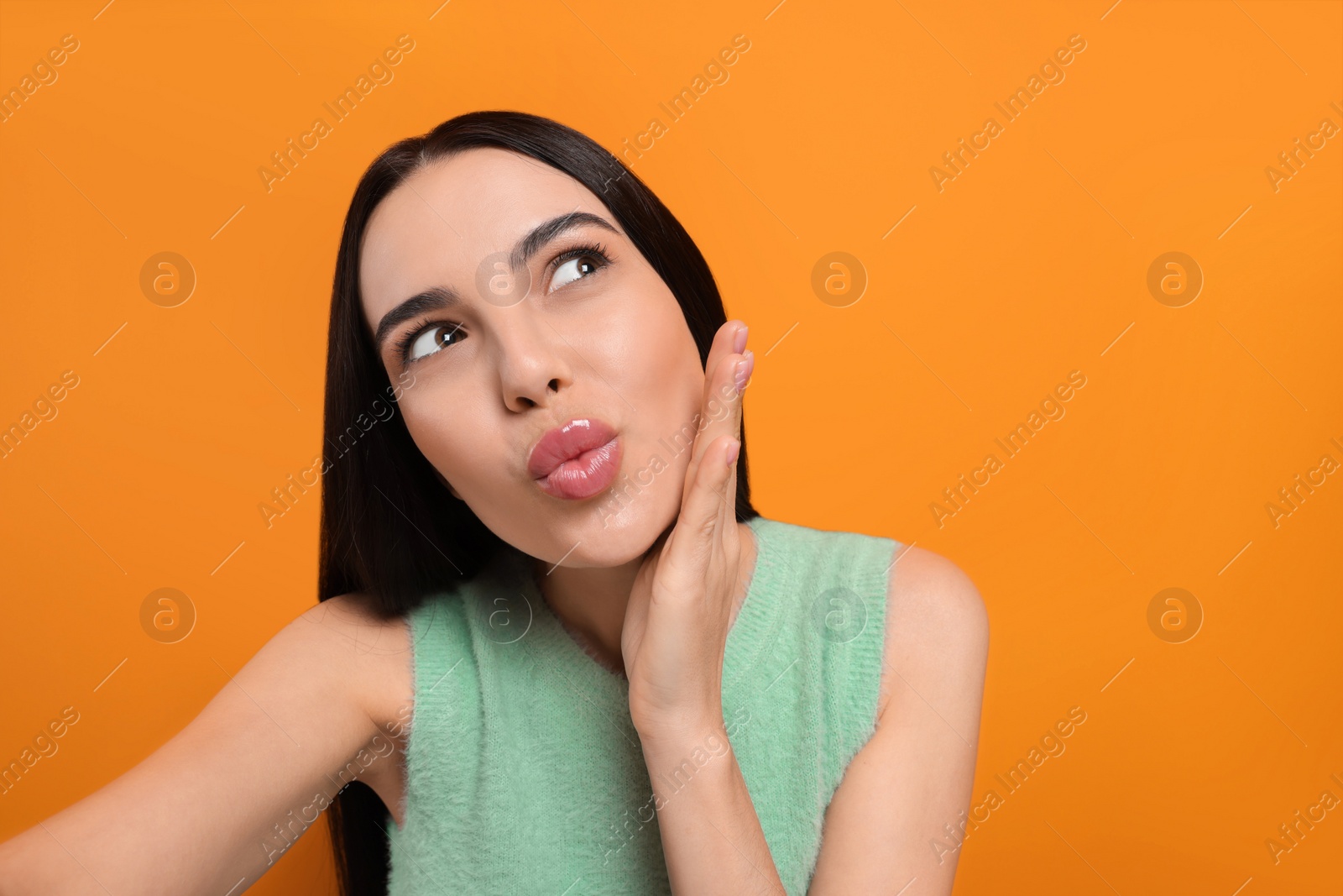 Photo of Beautiful young woman taking selfie while blowing kiss on orange background. Space for text
