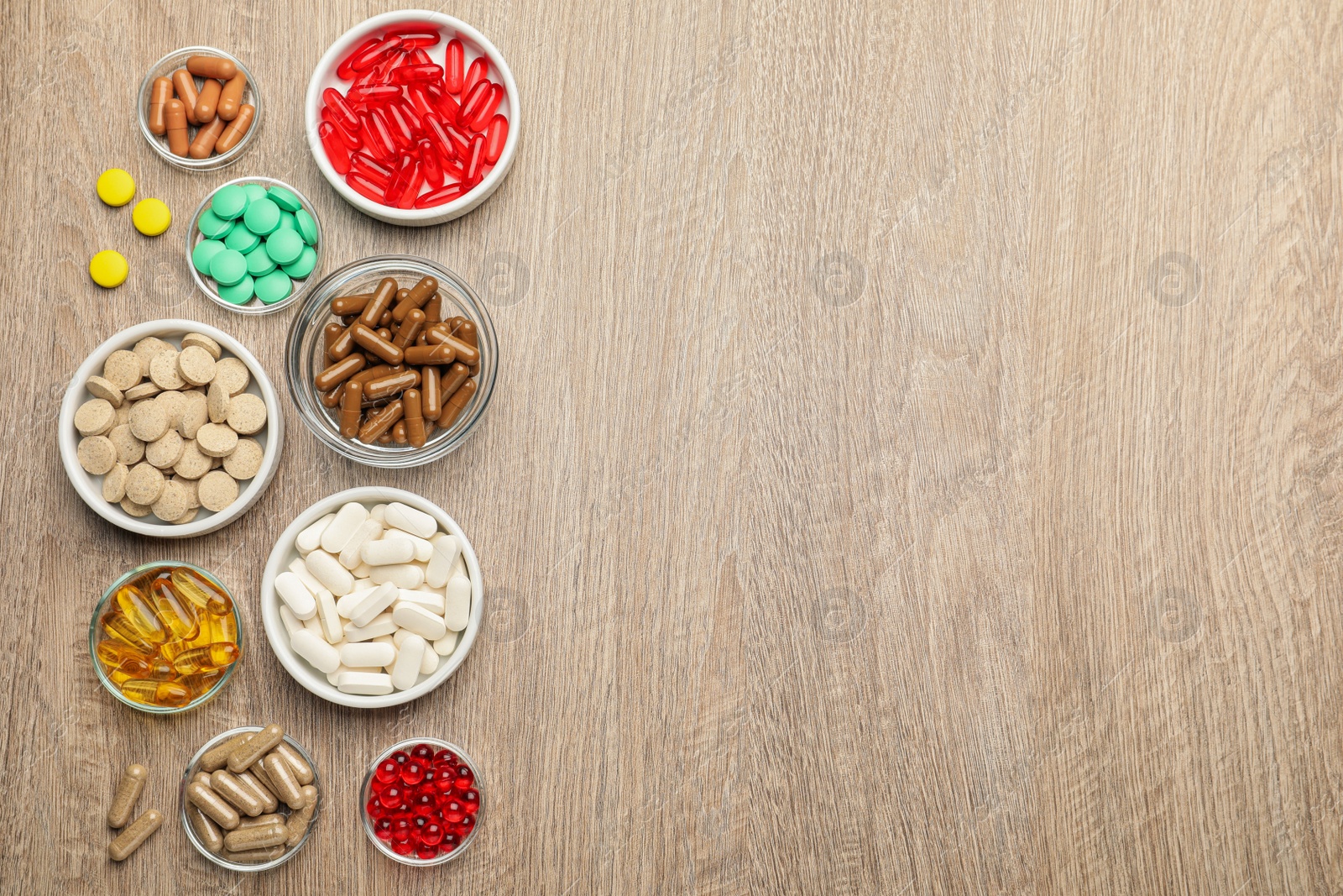 Photo of Different dietary supplements in bowls on wooden table, flat lay. Space for text