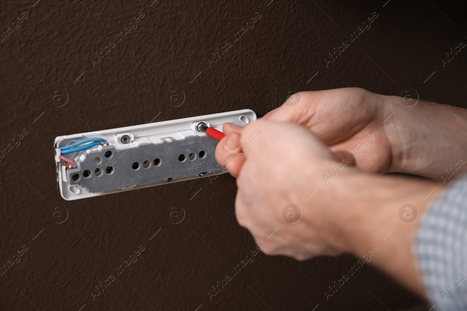 Photo of Electrician with screwdriver repairing power socket, closeup