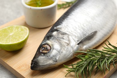 Wooden board with salted herring, lime, oil and rosemary on grey table, closeup