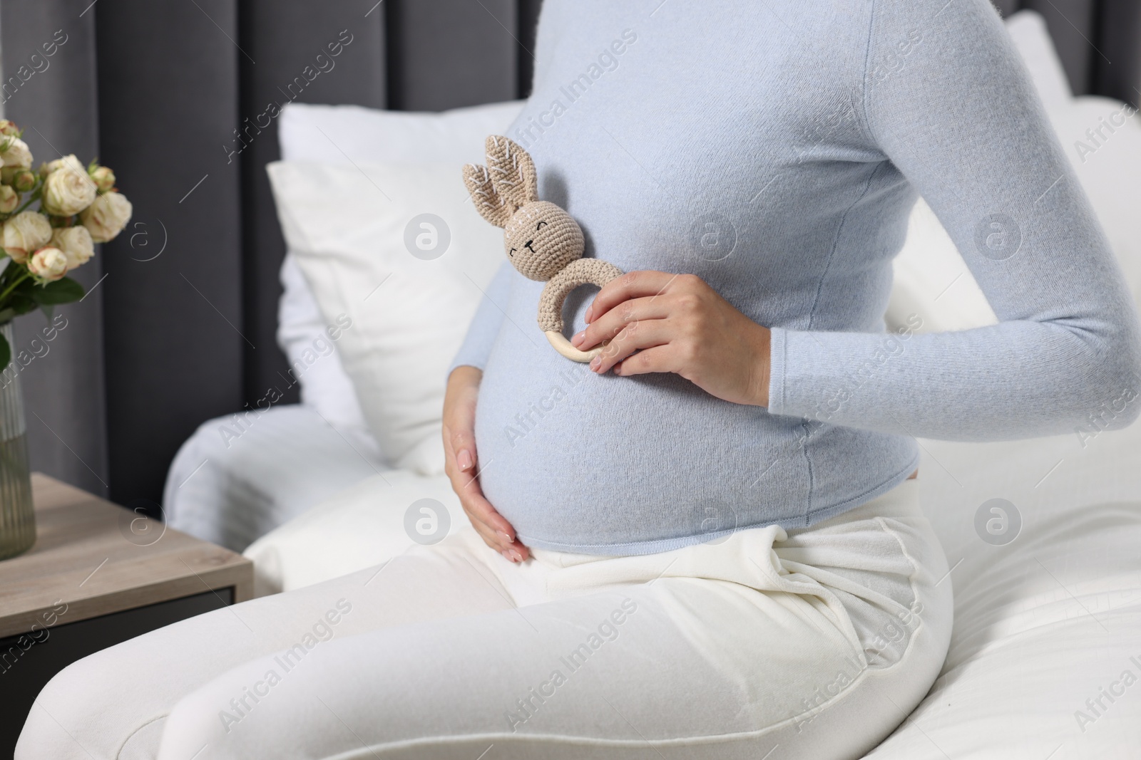 Photo of Pregnant woman with bunny toy on bed indoors, closeup
