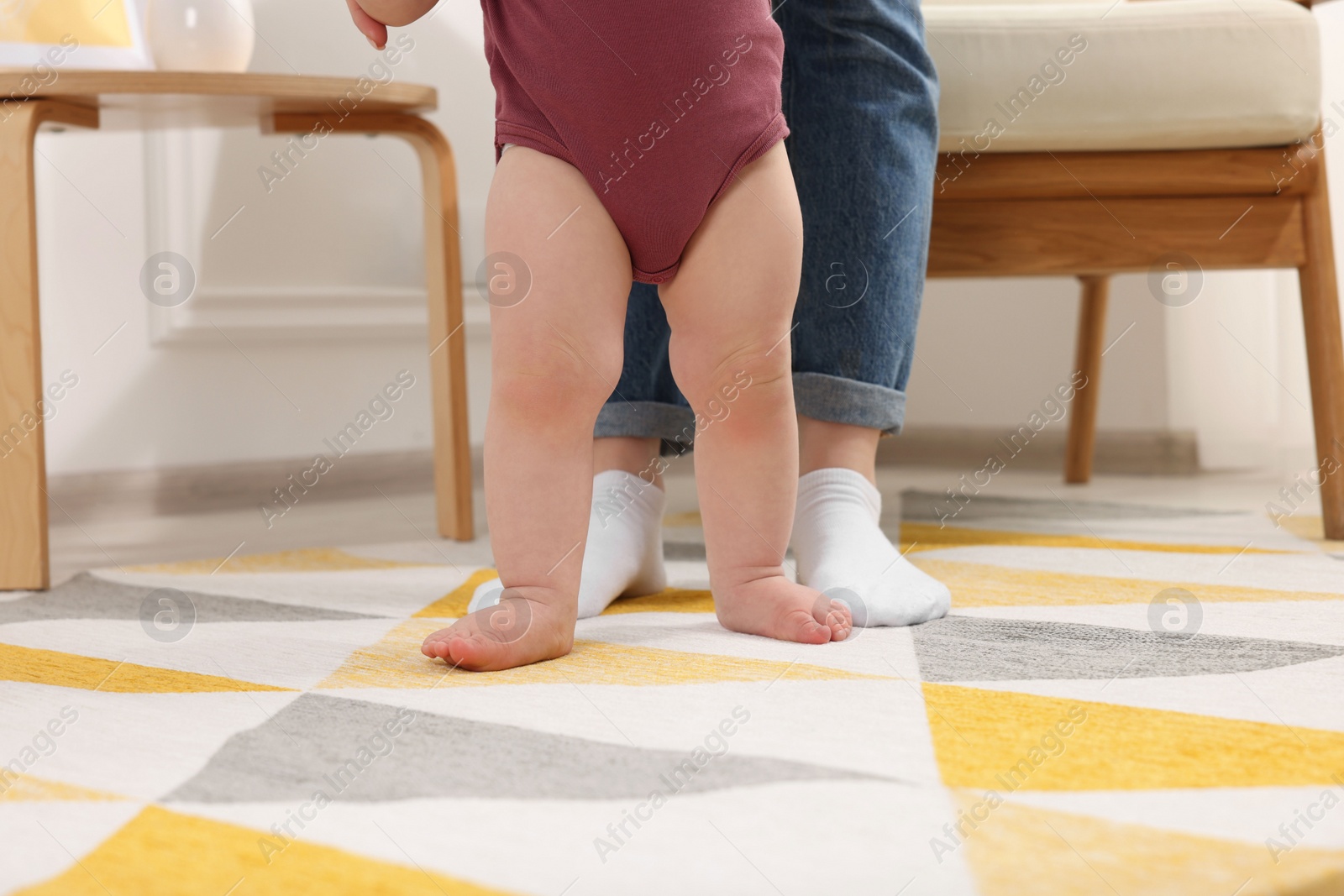 Photo of Mother supporting her baby son while he learning to walk on carpet at home, closeup