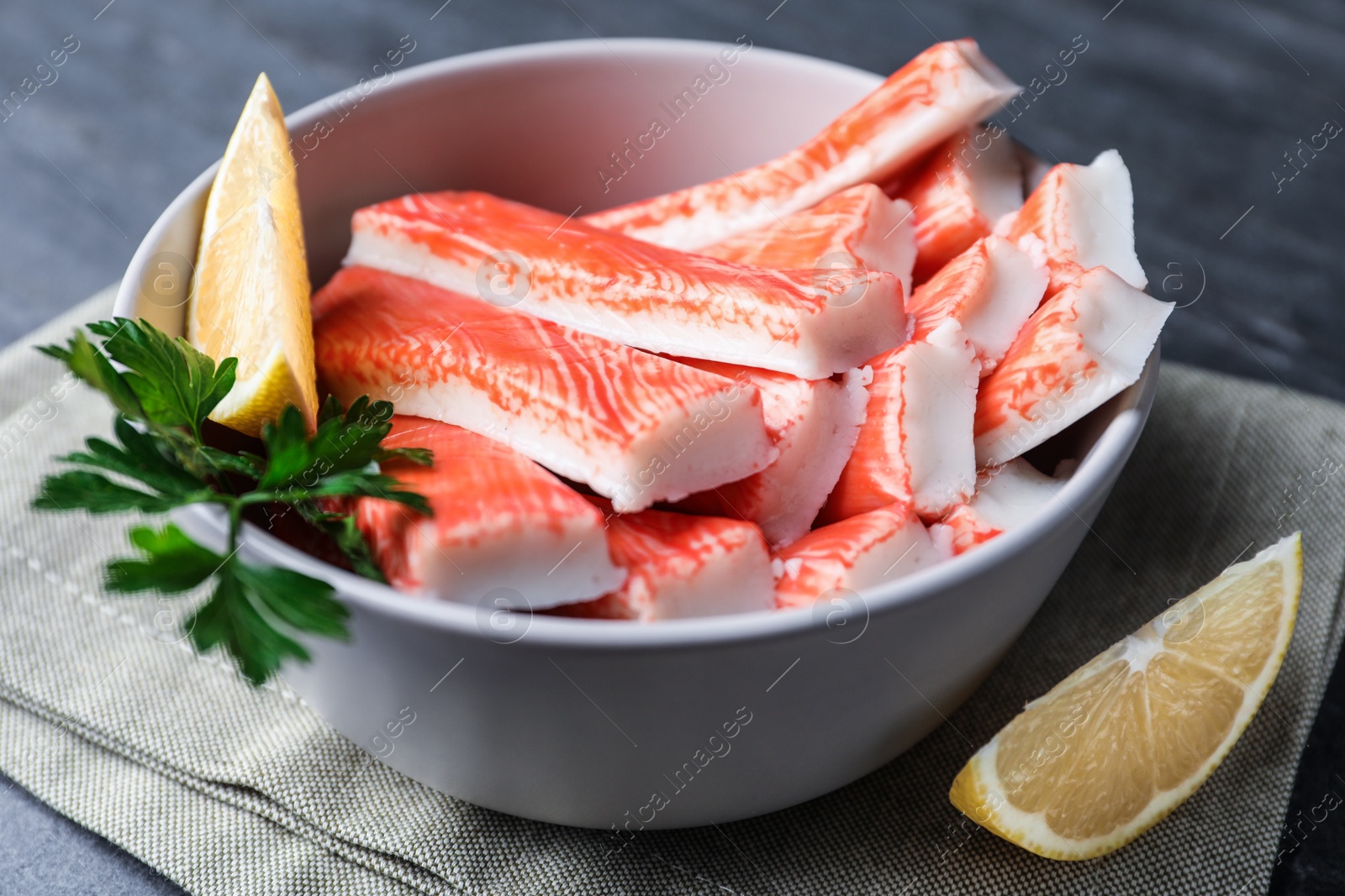 Photo of Crab sticks with lemon in bowl on grey table, closeup