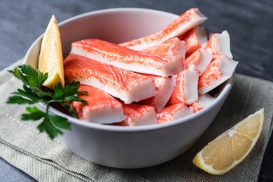 Photo of Crab sticks with lemon in bowl on grey table, closeup