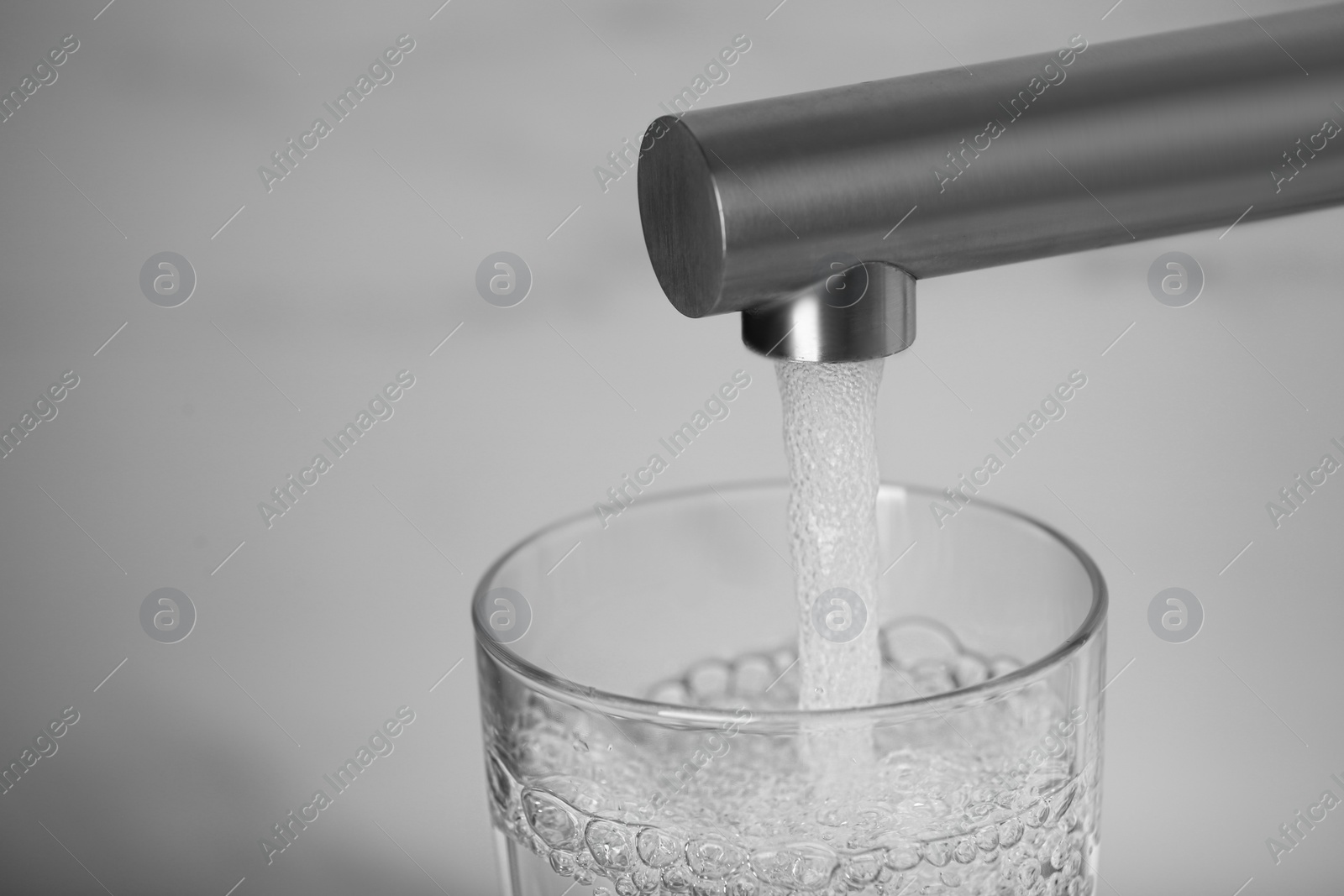 Photo of Filling glass with tap water from faucet on blurred background, closeup. Space for text