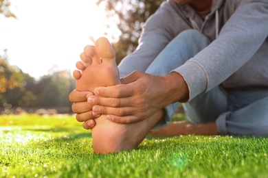 Man sitting barefoot on fresh green grass outdoors, closeup