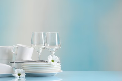 Photo of Set of many clean dishware, cutlery, flowers and glasses on light blue table. Space for text