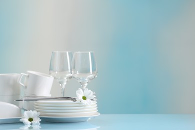 Set of many clean dishware, cutlery, flowers and glasses on light blue table. Space for text