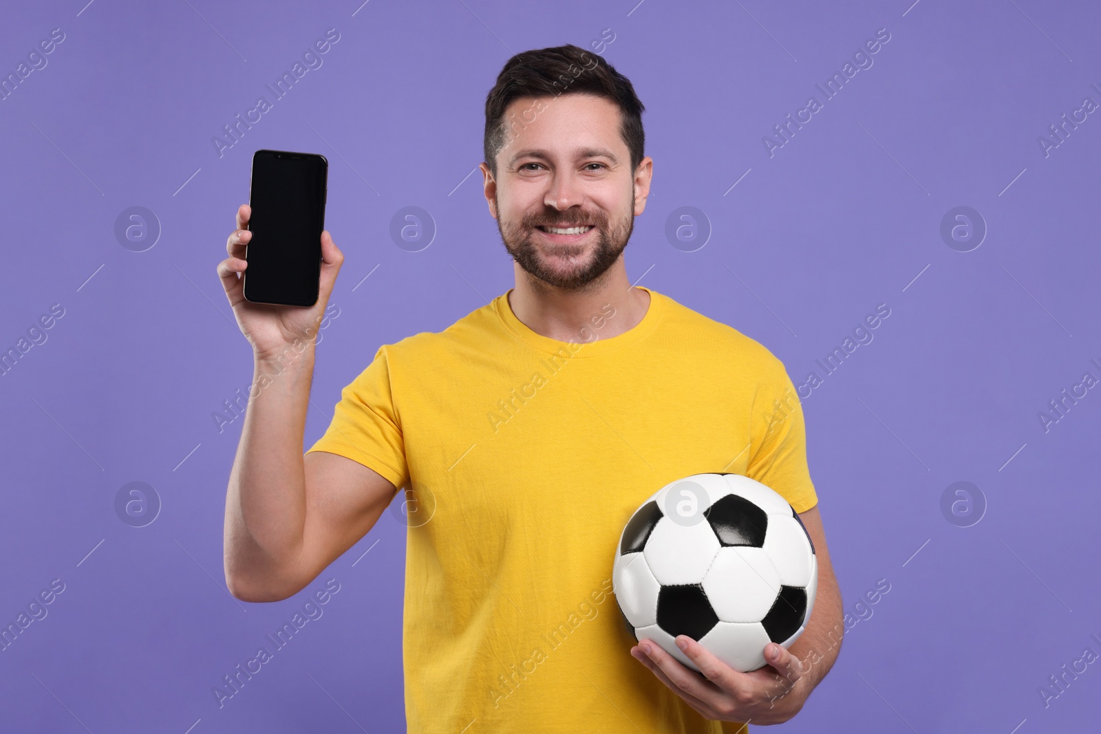 Photo of Happy sports fan with ball and smartphone on purple background