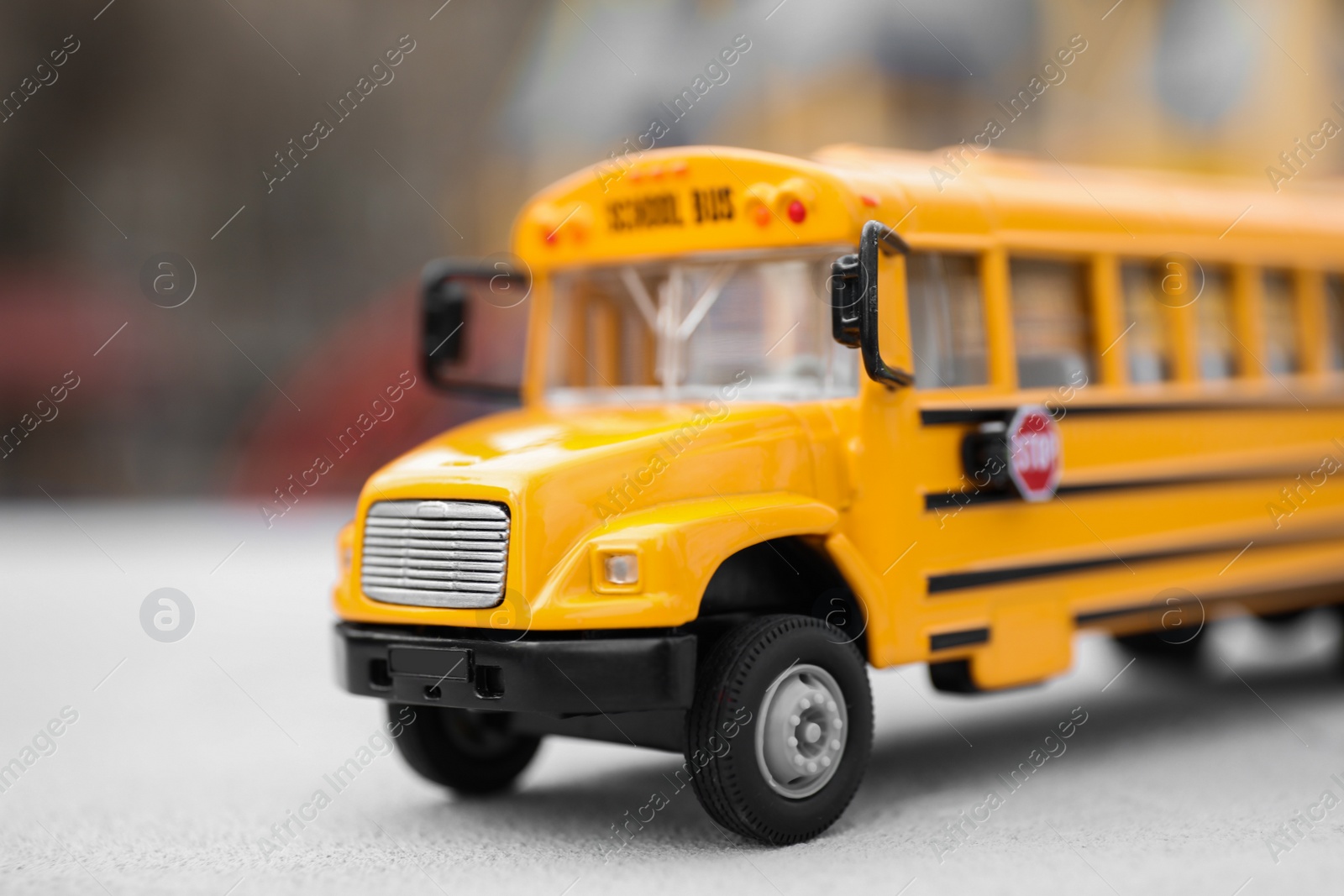 Photo of Yellow toy school bus against blurred 
background, closeup. Transport for students