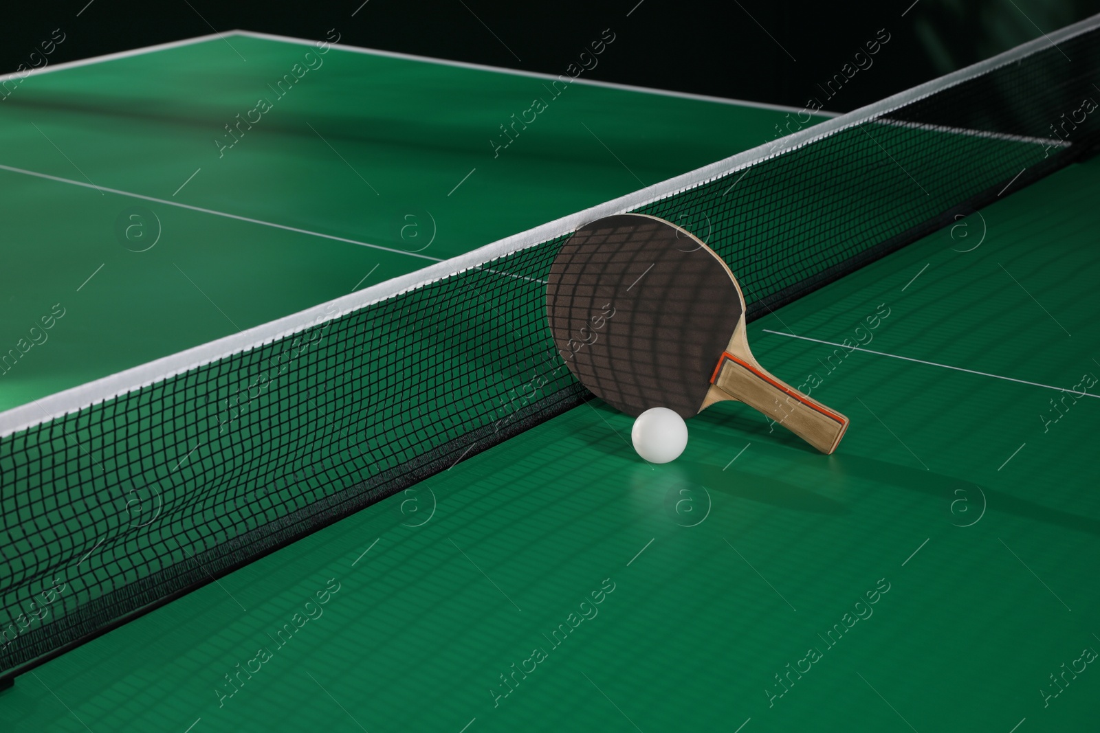 Photo of Black racket and ball on green ping pong table indoors