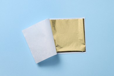 Photo of Edible gold leaf sheet on light blue background, top view