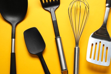 Photo of Different spatulas and whisk on orange background, flat lay