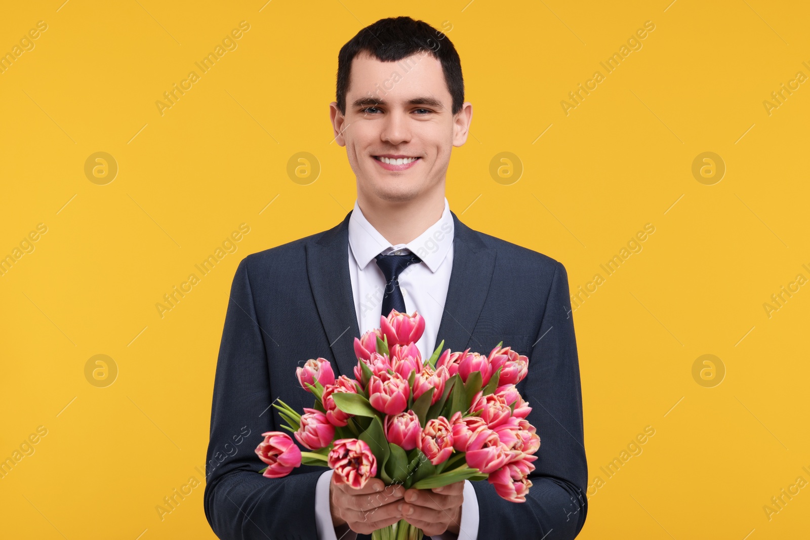 Photo of Happy young man with beautiful bouquet on orange background